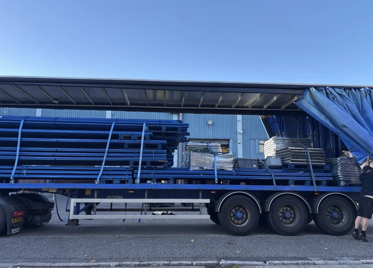 Pallet Racking Transport UK - Blue racking frames and bundled components on a curtain-sided trailer | UM Storage Systems