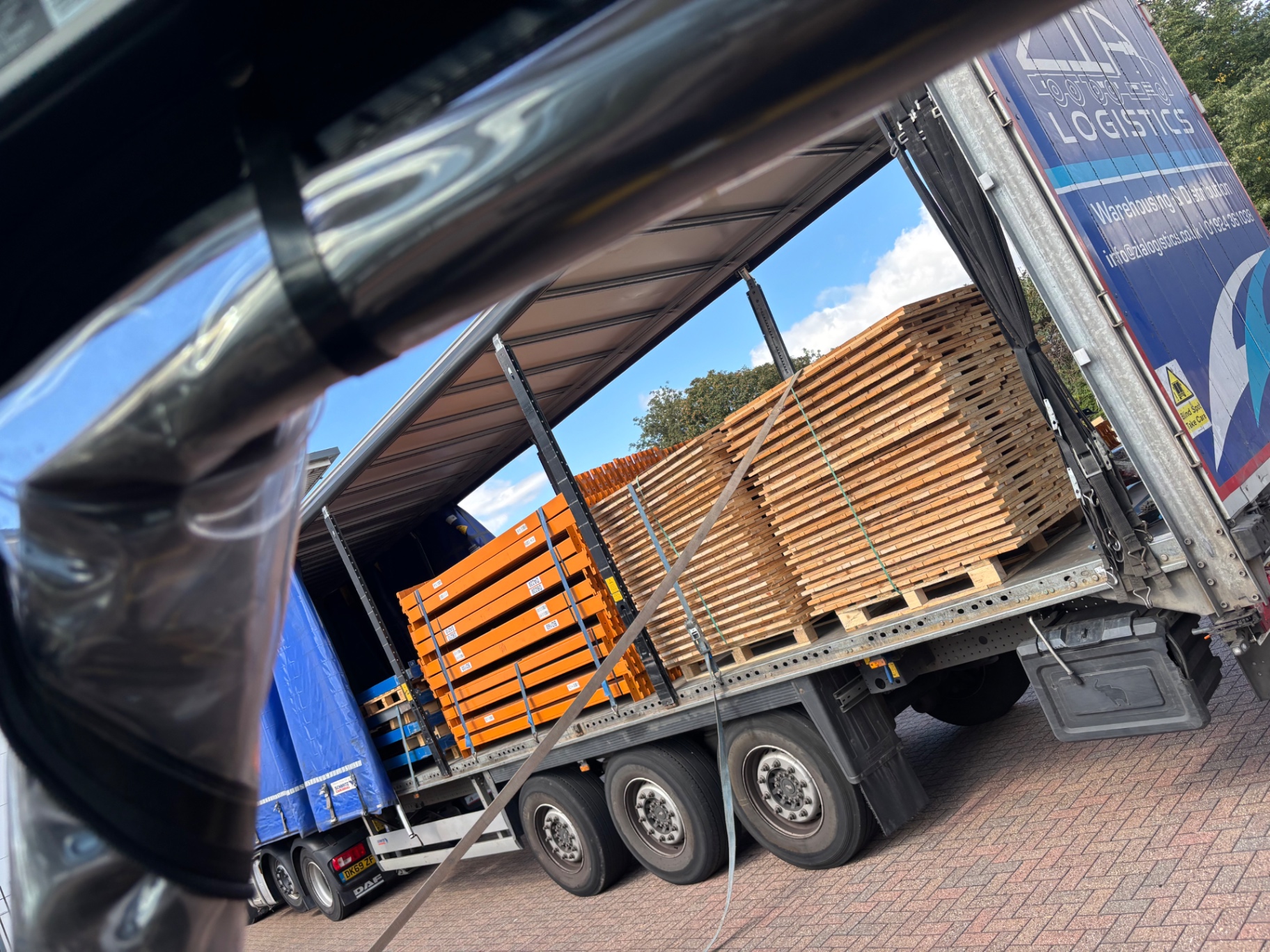 Pallet Racking Delivery UK - Orange beams and timber decking loaded on a curtain-side trailer | UM Storage Systems
